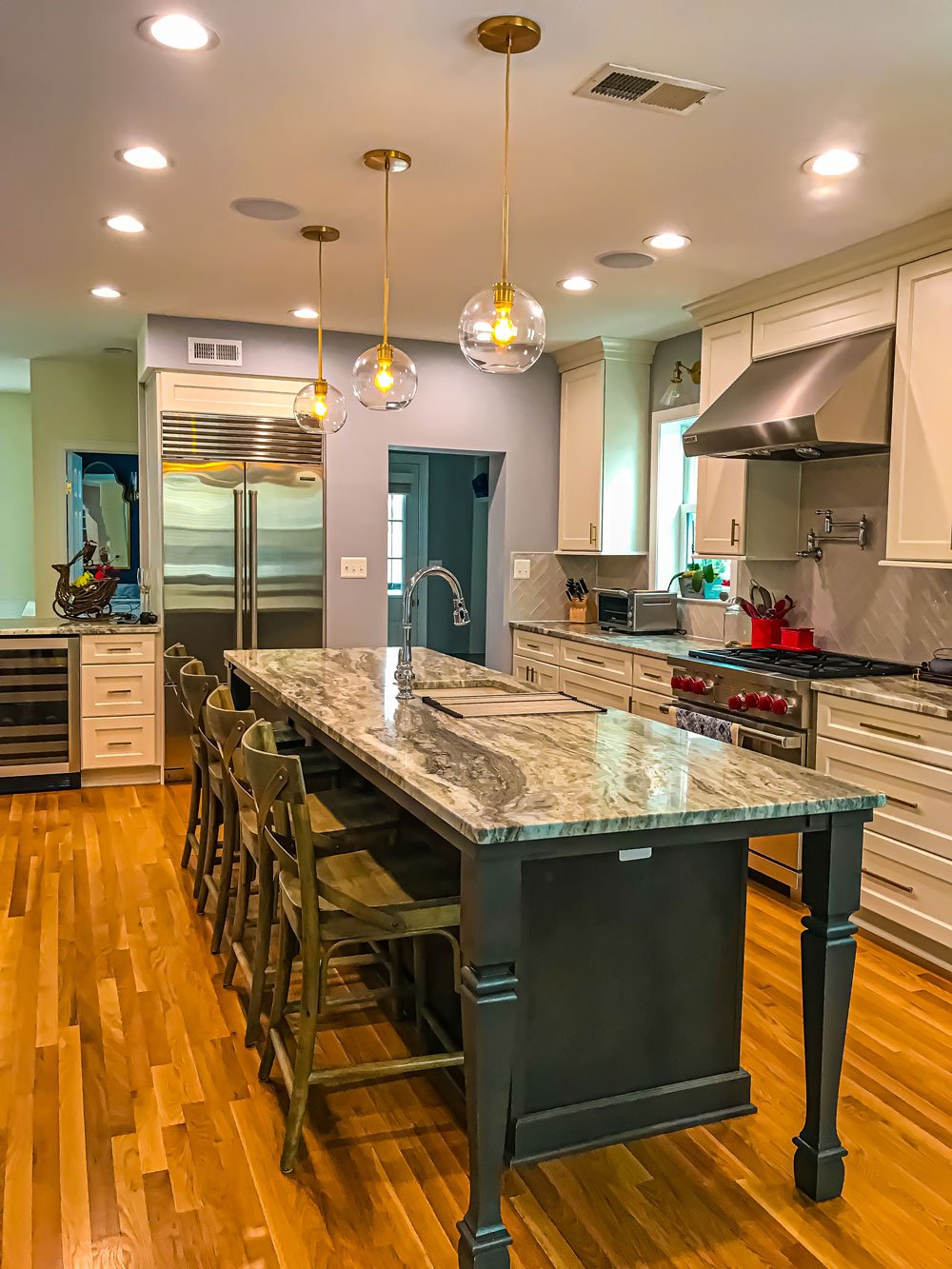 Long kitchen island with a grey/white marbled countertop and dark grey wood legs and cabinets