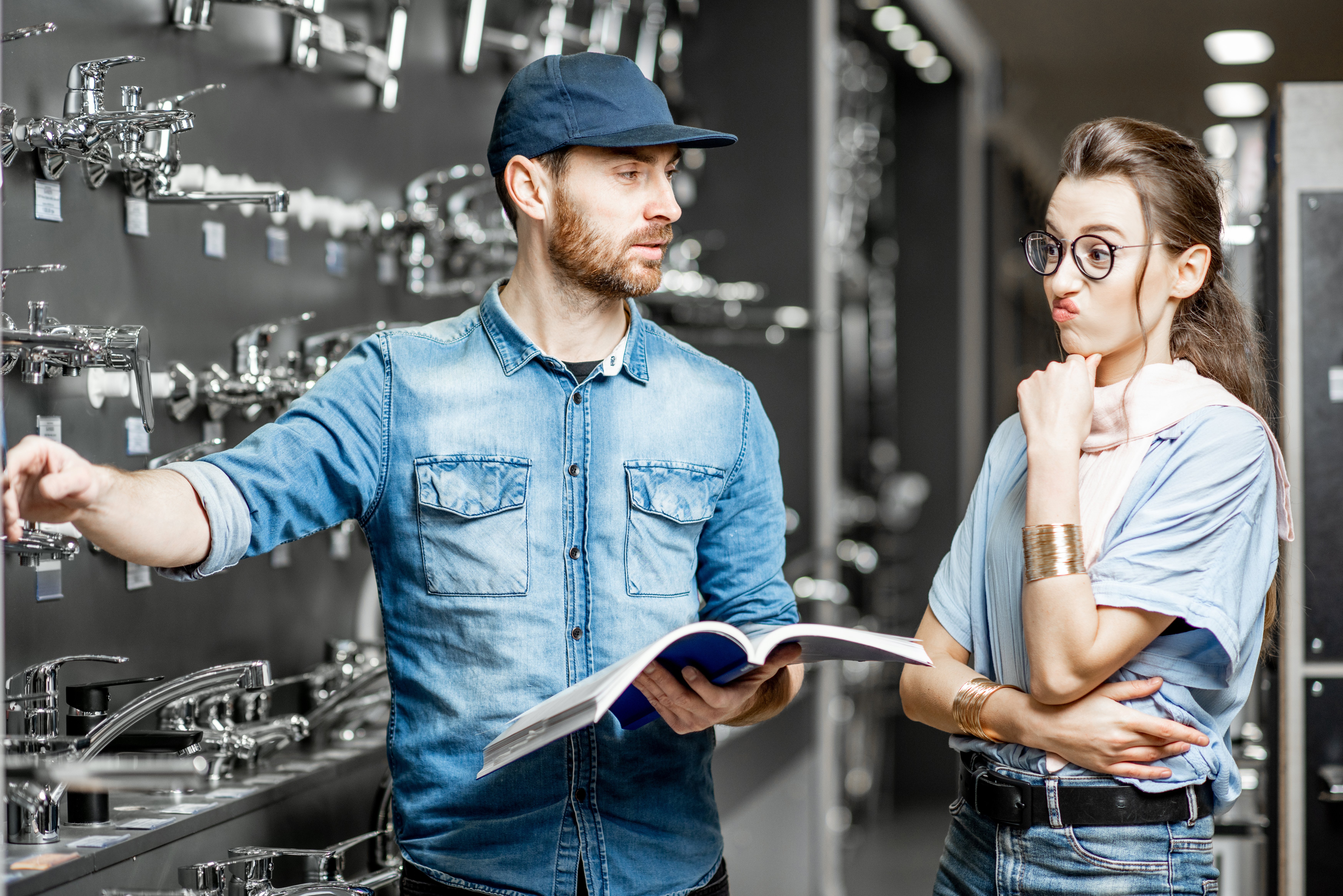 Man wearing a blue baseball cap and a denim shirt explains the selection process to a young woman planning a remodeling project