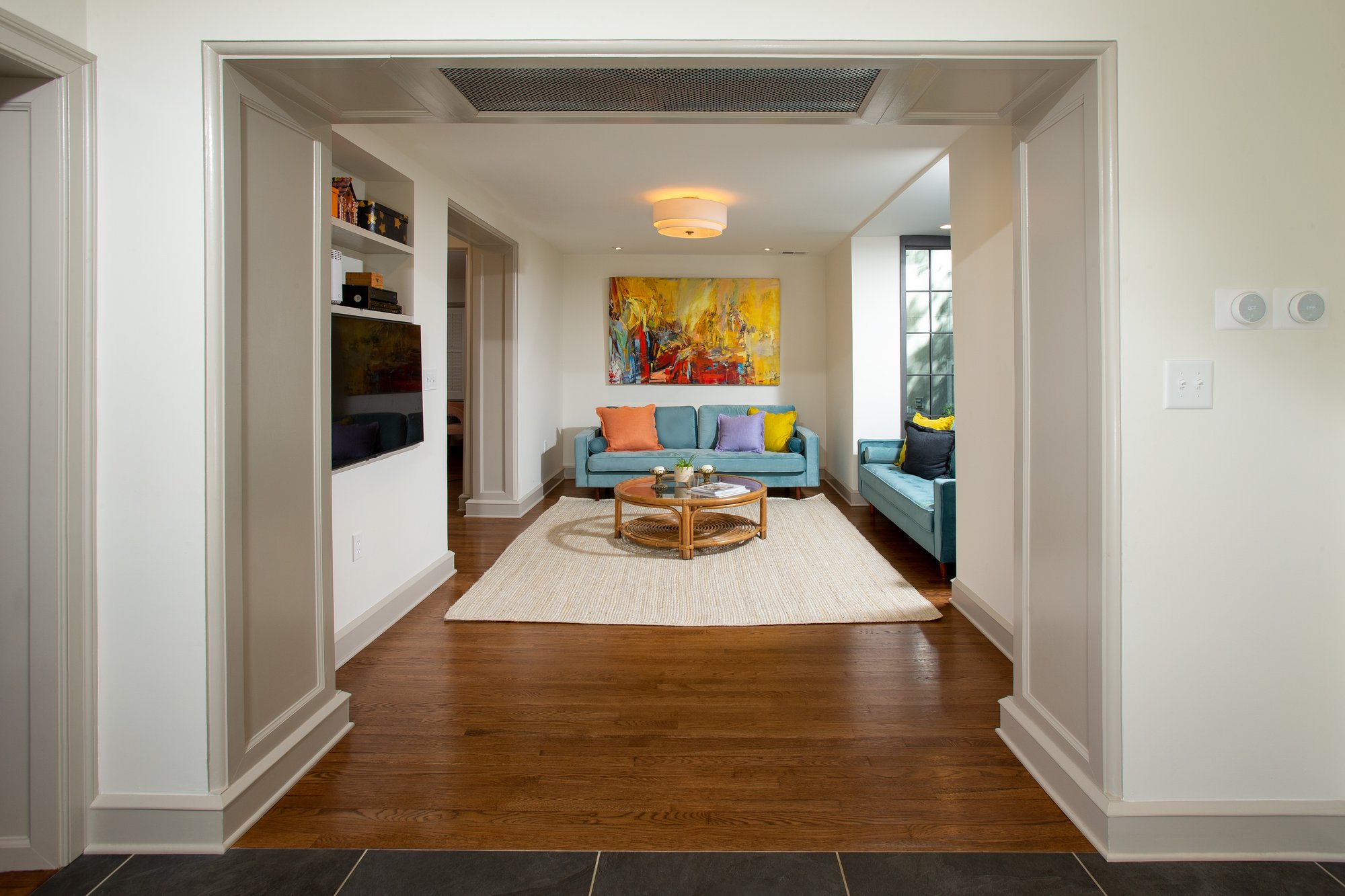 Front entrance and breezeway in residential home looking into a spacious living room with a wall mounted TV and baby blue furnishings