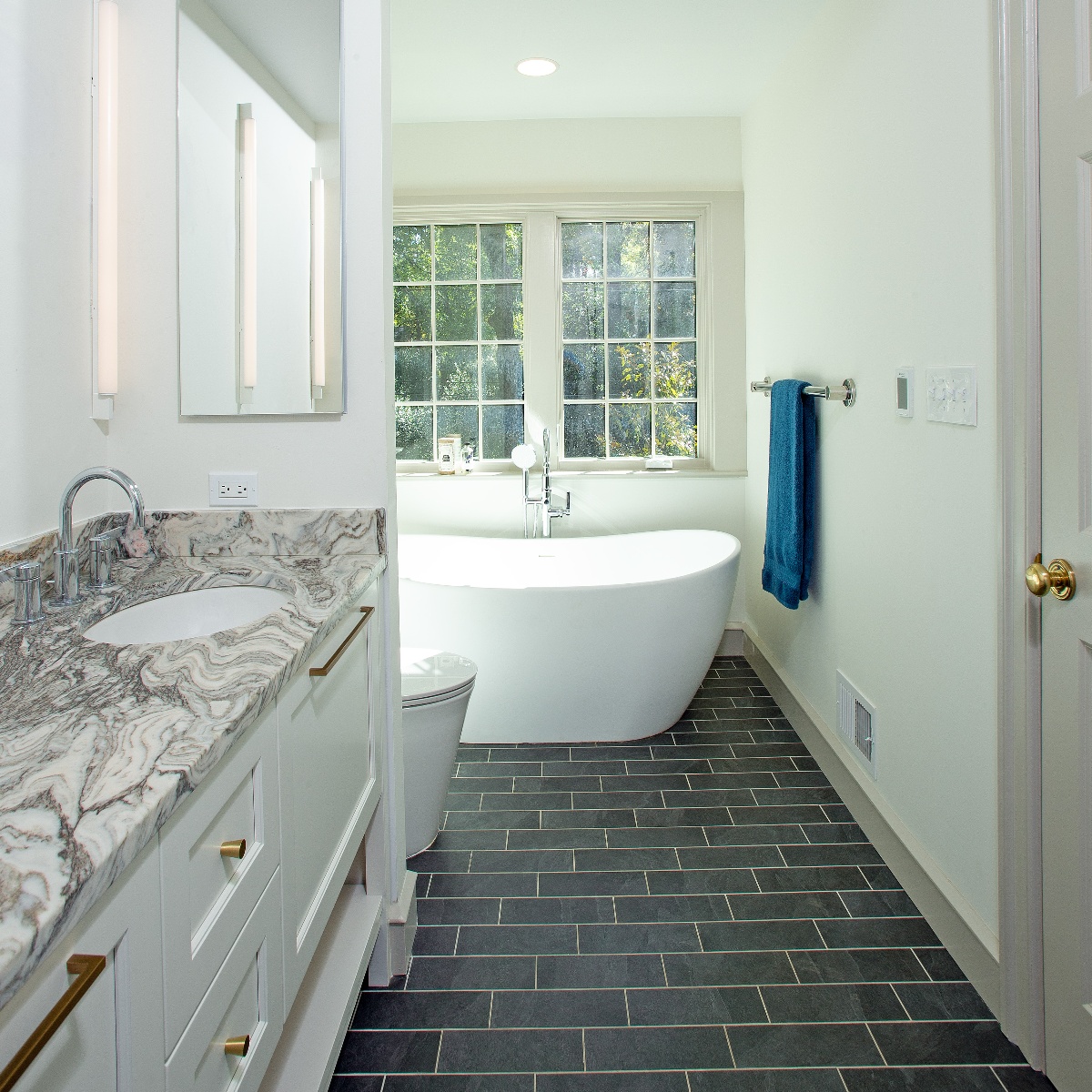 Black brick tile floored bathroom with stand alone tub in front of two paned window