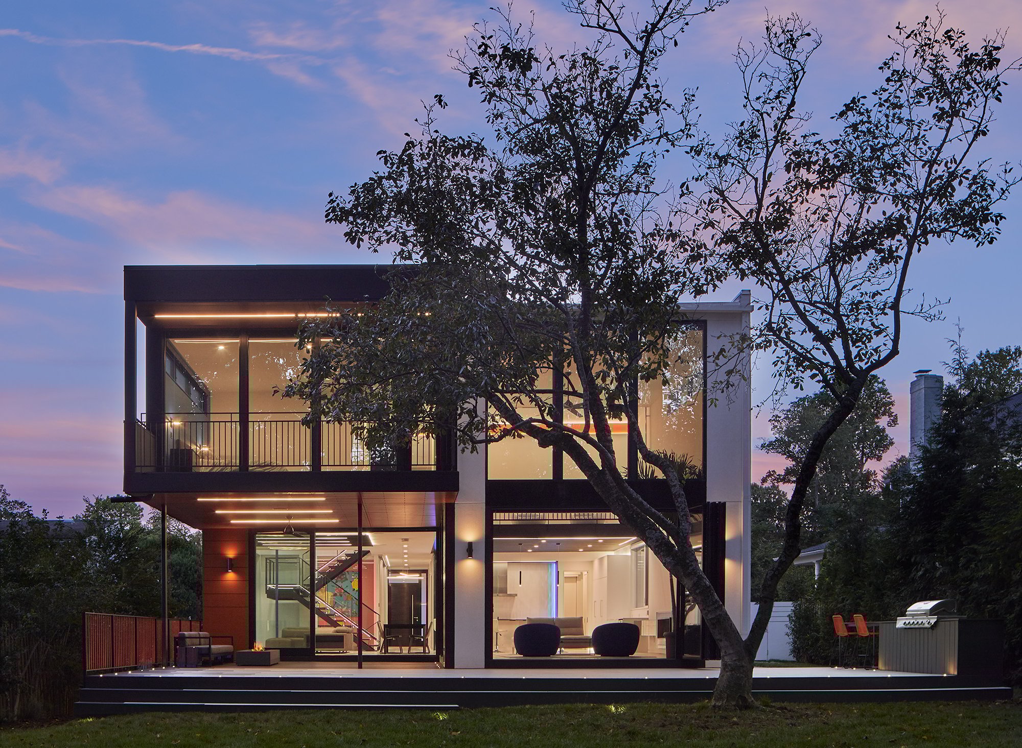 The back of a modern home during sunset.  A tree sits in the yard.