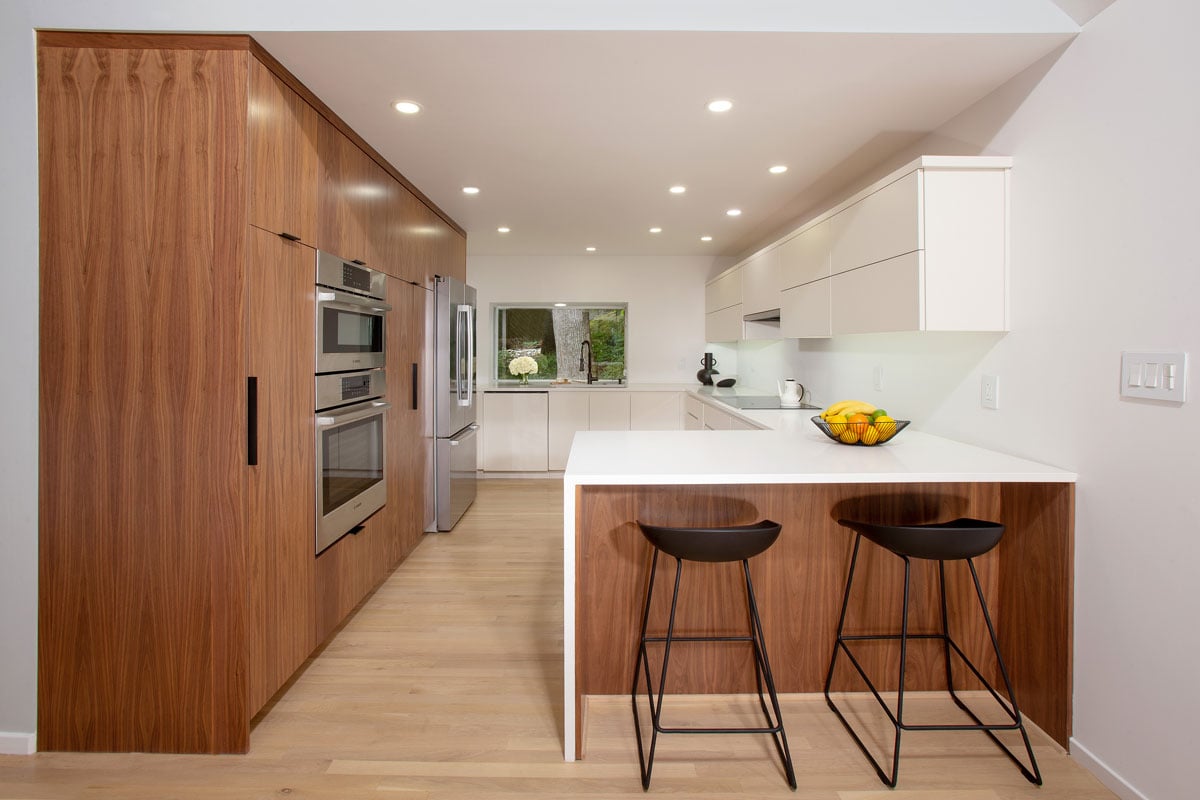 Natural stone kitchen island with two black stools look into a white and wood accented contemporary kitchen