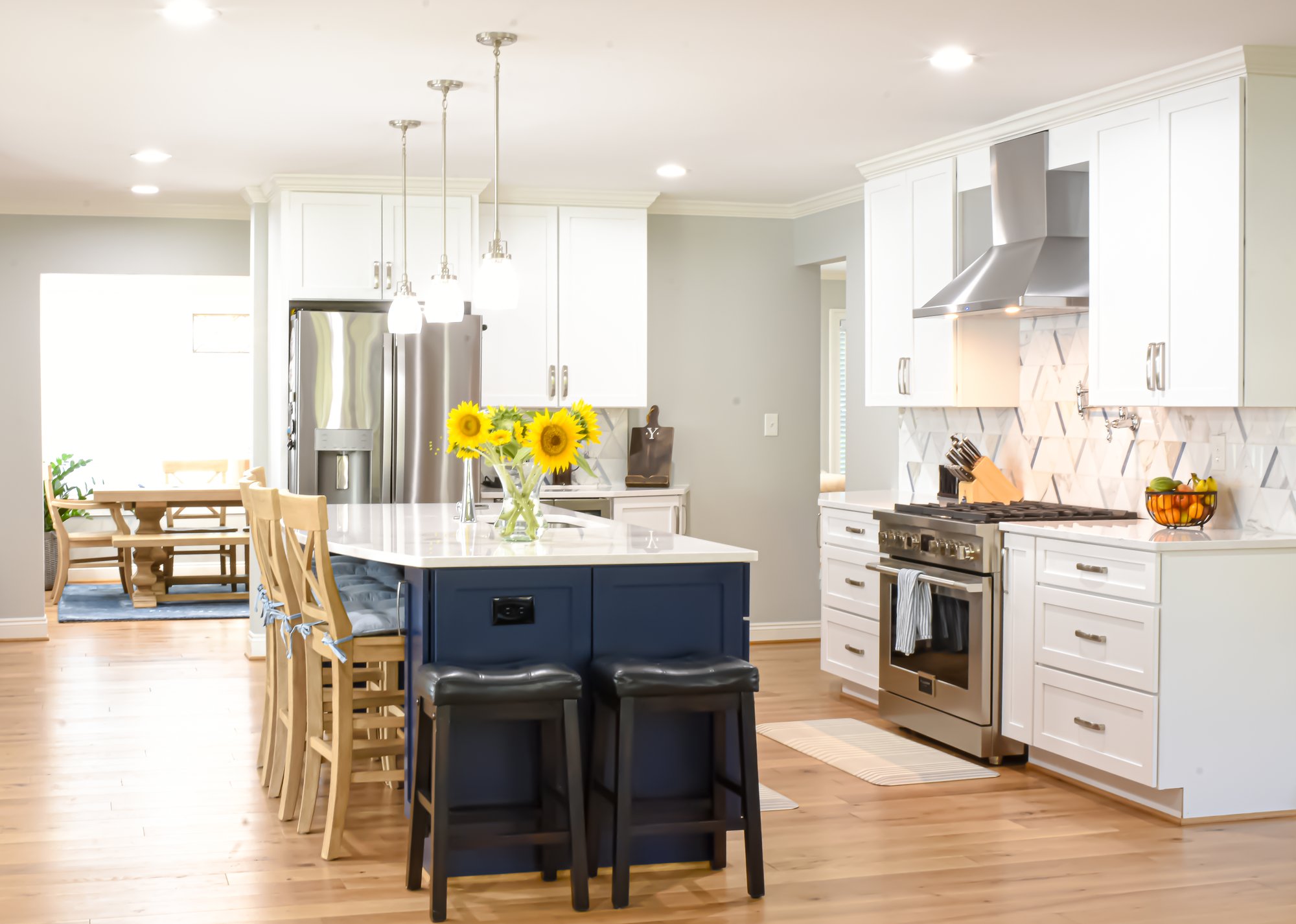 A large kitchen centered around a blue clad island sitting under three pendant lights.  The entrance to the dining room sits in the background.