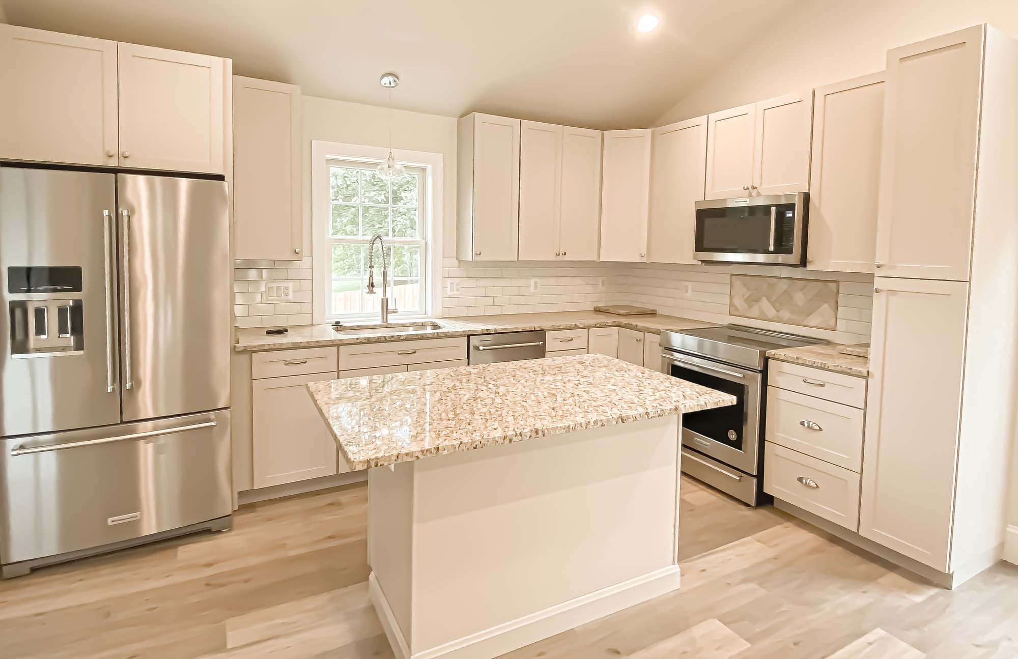 Simple and cozy kitchen with a small kitchen island, corner countertops, and stainless steel appliances. Luxury vinyl plank flooring