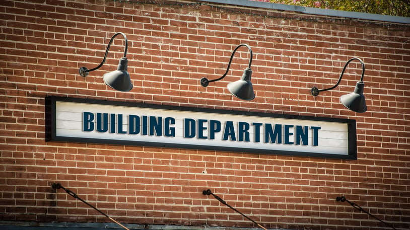 Brick wall department building with black lamps over a sign with bold, navy text