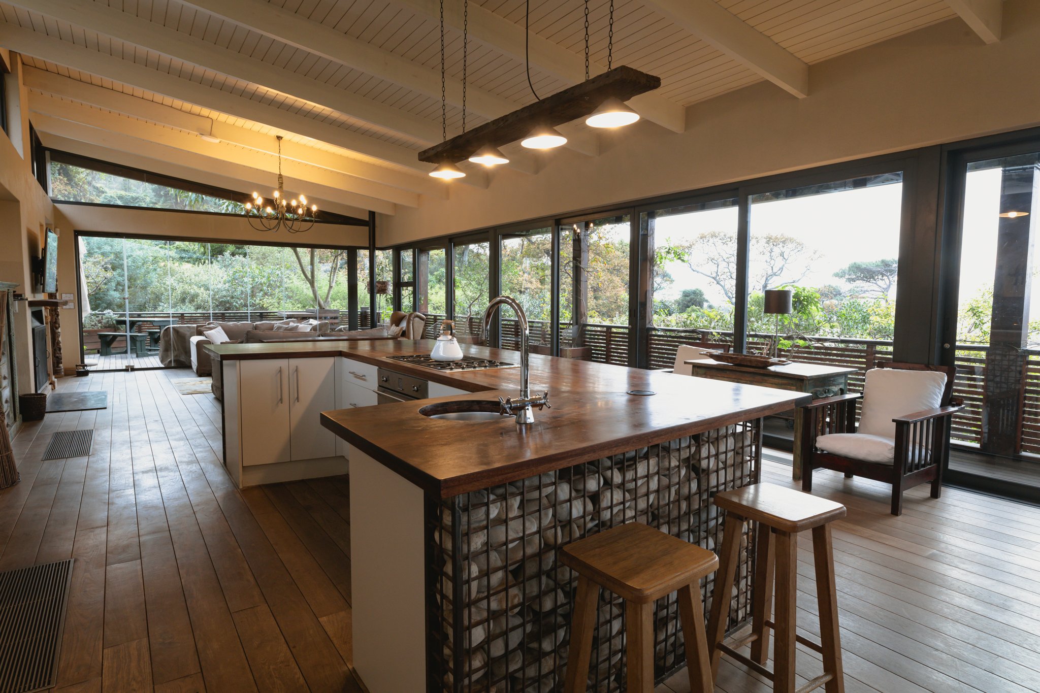 A open kitchen outfitted in dark wood and warm lighting with large windows facing the outside.