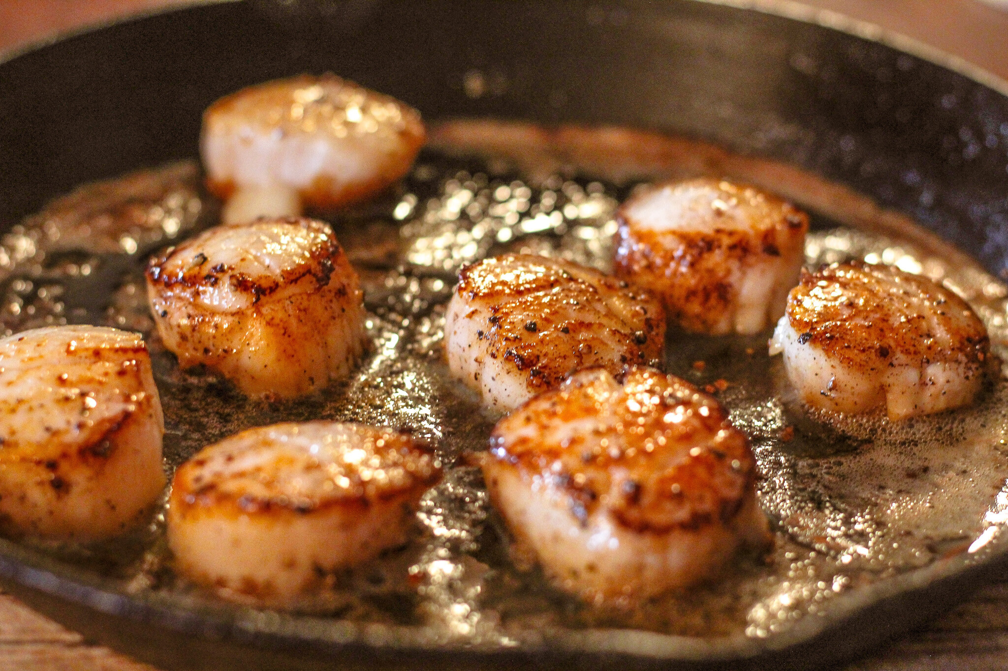 Scallops being seared in a pan with butter.