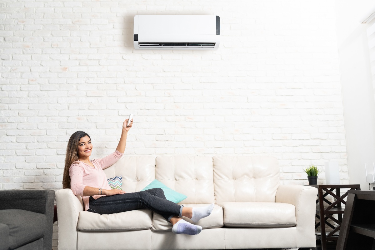 Woman sitting on a white leather couch with a mini-split heating and cooling system mounted above her on the wall