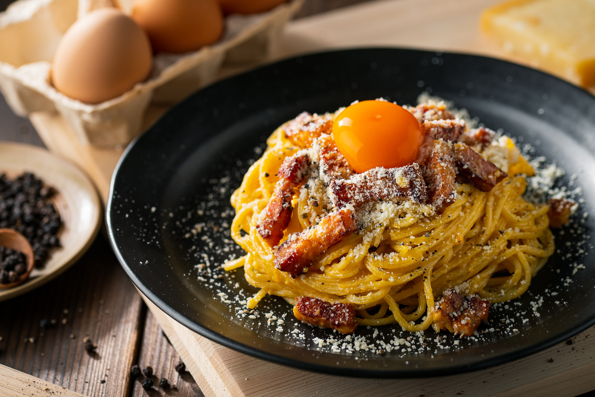 Carbonara pasta with an egg yolk sitting on top of a bed of spaghetti noodles and grated cheese.