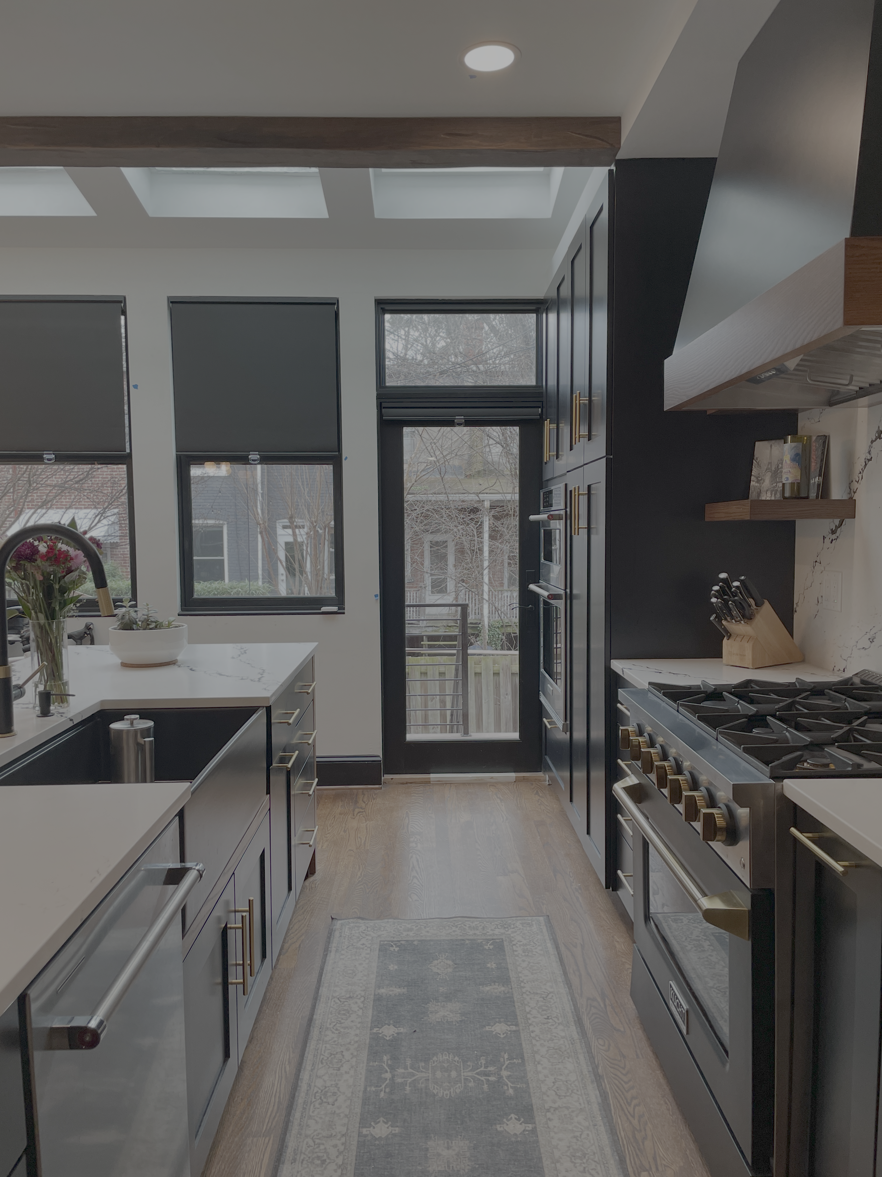 photo of a kitchen with black cabinetry, black appliances with brass accents and hardwood floors